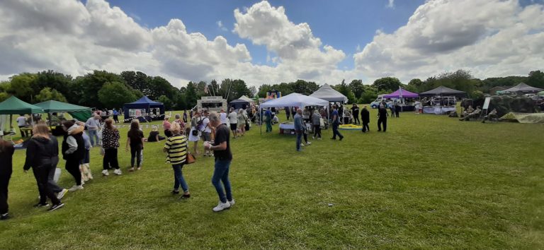 People gather on a green field. The sky is blue with white clouds.