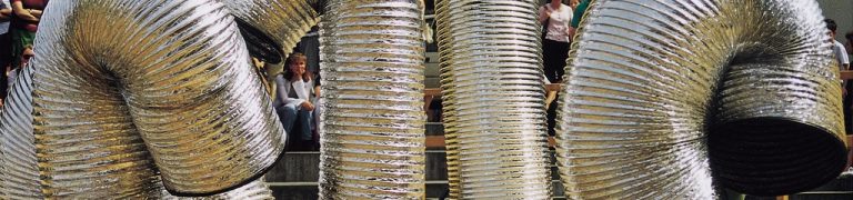 A photograph of a performance of Familie. Four large metallic slinkies create shapes during a street performance.