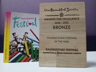 Basingstoke Festival bronze wooden award pictured next to the Basingstoke Festival 2024 brochure