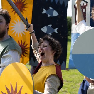 Three people are dressed as knights holding shields and swords.
