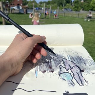 A close up photograph of a persons hand drawing in a sketchbook. The person uses a black pen on the paper. In the backdrop is a blurred playground with children playing.