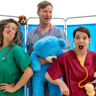 Three people are dressed as doctors in front of a screen and holding toy animals.
